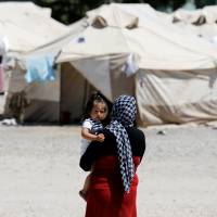 An Afghan migrant carries a child at a state-run camp for refugees and migrants in Schisto, near Athens, Monday. Angry asylum seekers torch migrant center on Greek isle