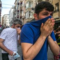 People cover their faces with T-shirts as Turkish anti-riot police fire rubber bullets to disperse demonstrators gathered for a rally staged by the LGBT community on Istiklal Avenue in Istanbul on Sunday. Istanbul riot cops break up Trans Pride event