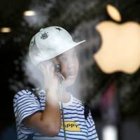 A youth uses a phone in an Apple store in Beijing Wednesday. Apple sees slump in iPhone sales but marks billionth in circulation