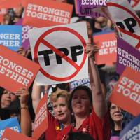 People hold up signs against the Trans-Pacific Partnership trade deal on Wednesday at the Democratic National Convention in Philadelphia. Obama to push for Congress to pass TPP despite its demonization in campaign