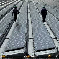 Workers walk among the rows of solar panels at Kyocera Corp.’s floating solar power plant in Saka Sama Lake in Kasai, Hyogo Prefecture, in May 2015. Sun no longer shines on Japan's solar boom as subsidies wane