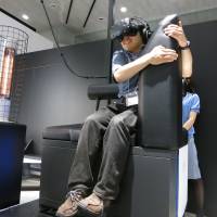 A gamer wears a headset during a virtual reality battle from the safety of Gundam’s palm, at VR Zone Project i Can in Tokyo’s Odaiba district on Thursday. A heat lamp adds realism. Tokyo VR attraction puts you in the heart of a Gundam battle