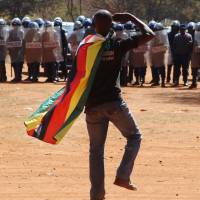 A man wearing a Zimbabwean flag salutes riot police during a protest in Harare on Friday. Mugabe tells Zimbabwe protesters they are doomed to fail