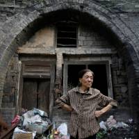 Li Yonghua, 65, stands in front of her damaged cave house in an area where land is sinking next to a coal mine in the village of Helin in China's Shanxi province on Aug. 2. Undermining China: towns sink after mines close