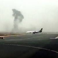 This image made from video shows smoke rising after an Emirates flight crashed on landing at Dubai International Airport on Wednesday. The plane at right was unaffected Dubai-based airline Emirates has confirmed that there were no fatalities on the flight from India that crashed. Wind shear reported as Emirates 777 breaks up, burns on landing; all 300 aboard safe, firefighter dies