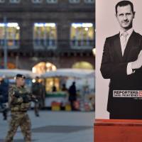 A French soldier walks past a poster of Syrian strongman Bashar Assad showing off his middle finger in Strasbourg, France, last November. The poster was sponsored by the nonprofit organization Reporters Without Borders. U.N. defends aid work in Syria after accusations of being too close to Assad government
