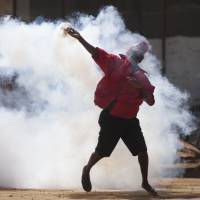A supporter of the Zimbabwean opposition party Movement for Democratic Change hurls a tear gas canister back at police as protesters clashed with them during a march against police brutality in Harare on Wednesday. Zimbabwe police fire tear gas, beat anti-Mugabe marchers in capital