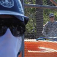 Heavy presence: As private security guards stand outside, a U.S. soldier watches through the fence from inside the site where new helipads are being built within the U.S. Marine Corps Northern Training Area in northern Okinawa. U.S. washes hands of rights violations at Okinawa helipad site