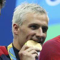 Ryan Lochte (USA) bites his gold medal after the men’s 4×200-meter freestyle relay final in the Rio 2016 Summer Olympic Games at Olympic Aquatics Stadium on Aug. 9. Rio cops seek to quiz cabby over robbery by apparent police of U.S. swimmer Lochte, teammates