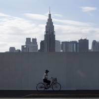 A cyclist passes the construction site of the new National Stadium in Tokyo, set against the Shinjuku skyline. Land prices cease falling in Japan amid demand for tourist infrastructure