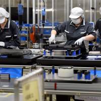 Workers assemble analog record players on an assembly line at Panasonic's Utsunomiya plant in Tochigi Prefecture on Wednesday. OECD cuts world growth outlook amid weak advanced economies