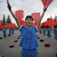 North Korean women wave flags cheering on their fellow countrymen as they start their day during morning rush hour Wednesday in Pyongyang. Leading female activists petition U.N. chief to pursue Korea peace treaty