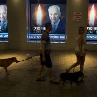 Israelis walk their dogs next to screens displaying a photo of former Israeli President Shimon Peres in Tel Aviv Wednesday. The country mourned the death of Peres, a former president and prime minister whose life story mirrored that of the Jewish state. Obama to attend Jerusalem funeral for Shimon Peres