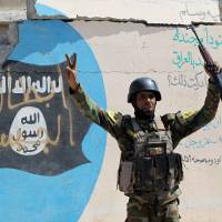 An Iraqi government soldier celebrates in front an Islamic State group flag covered in graffiti in the town of Sharqat, around 80 km (50 miles) south of Mosul, Iraq, on Friday. Iraq oil fires could jeopardize mission to retake Mosul from Islamic State forces