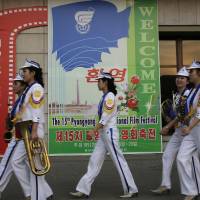 North Korean band members who performed at the Pyongyang International Film Festival walk past a sign at the venue where it was held Friday in the North Korean capital. Film about selfless woman who helps orphans takes top spot in North Korean festival