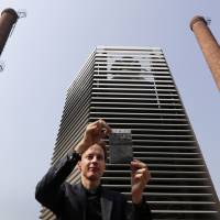 Dutch artist Daan Roosegaarde shows smog particles collected by the Smog Free Tower on display between chimney stacks as he presents his machine at D-751 art district in Beijing on Thursday. Smog Free Tower opens in pollution-prone Beijing