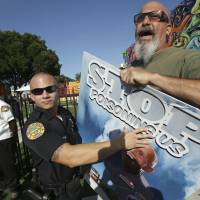 A Miami police officer holds back protestor Judd Allison as Florida Gov. Rick Scott leaves a news conference at Wynwood Walls, Monday in Miami. The governor said the arts district is no longer considered a zone of active Zika transmission. Allison was protesting the use of the pesticide naled, which was used in the area to combat Zika. Zika threat eases for part of Miami as Congress grapples to clear way for long-delayed funds