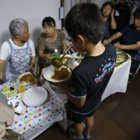 A boy ladles curry onto a plate at a kodomo shokudo (children's cafeteria) in Tokyo on Aug. 18. Misako Omura's weekly dinner is one of a growing number of such initiatives springing up across Japan. Children's cafeterias serving food, support to kids in need