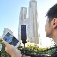 A Ricoh Theta S camera (mounted on stick) is used to take 360-degree photos near the Tokyo Metropolitan Government building in Shinjuku Ward on Aug. 31. The image can be transmitted to a smartphone for viewing. Tech world wraps head around 360-degree photography