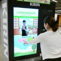 A customer takes a selfie using a camera-equipped vending machine in Osaka made by Kirin Beverage Co. in August. The machine will send the photo to her smartphone. Smartphone-linked vending machines on rise as drink makers thirst for sales