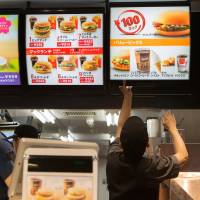 Going down?: An employee changes a sign at a McDonald's in Tokyo after prices were cut in 2014. Since then, more discounts have been added to its menu. Are bargain burgers quickening Japan's deflationary tailspin?