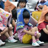 Welcome to September: Elementary school children wearing fireproof hoods gather in their playground as part of a nationwide earthquake drill at a Tokyo elementary school on Disaster Preparedness Day, Sept. 1. | AFP-JIJI