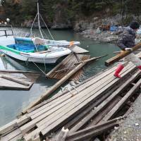 A fisherman cleans up the wreckage of a pier destroyed by tsunami in Higashimatsushima, Miyagi Prefecture, on Nov. 23. Tohoku fisheries elude major damage from March 2011 aftershock