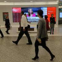 Passersby watch the performance of stocks on a financial news television screen in the business district of Toronto Monday. 'Fear gauge' up as Trump travel curbs send stocks, dollar down sharply
