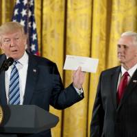 President Donald Trump, accompanied by Vice President Mike Pence, holds up a letter left for him by former President Barack Obama as he speaks at a White House senior staff swearing-in ceremony in the East Room of the White House Sunday in Washington. Trump drops caustic tone, vows to really govern fairly, embraces Comey