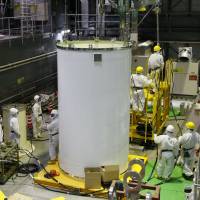 Workers check a transport container and a crane in preparation for the removal of spent nuclear fuel from a pool at No. 4 reactor building of Tepco’s Fukushima No. 1 nuclear power plant in Okuma, Fukushima Prefecture, in November 2013. Law to make Tepco retain money for decommissioning costs
