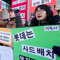 South Korean protesters hold signs during a rally against the planned deployment of a U.S.-built anti-missile system, outside Lotte International in Seoul on Monday. China threatens boycotts after South Korea missile defense decision