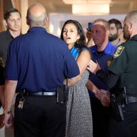 A protester (center) is escorted away from a Wells Fargo annual shareholder meeting by hotel security and police officers in Jacksonville, Florida, Tuesday. Wells Fargo faces angry shareholders, protesters but board stays on