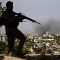 A member of the Iraqi forces stands guard over a building in the eastern section of the Iraqi city of Mosul, as smoke rises from the Old City during an offensive to retake it from Islamic State group fighters. Islamic State massacres dozens of civilians trying to flee Mosul, witnesses say