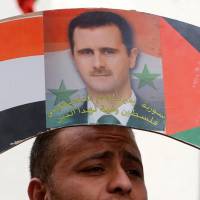 A Palestinian demonstrator holds a placard with a poster depicting Syrian President Bashar Assad during a protest against U.S. airstrikes in Syria, in the West Bank city of Nablus, on Sunday Assad may see U.S. strike as only 'a slap on the wrist'