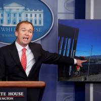 Director of the Office of Management and Budget Mick Mulvaney points to a picture of construction of the southern border while speaking about the budget agreement reached by Congress during a press briefing at the White House in Washington Tuesday. Health bill again teeters but House OKs $1.1 trillion budget bill