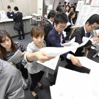 Company employees distribute press releases on their earnings last week at the Tokyo Stock Exchange. Japanese firms' net profits surged 21% in fiscal 2016: analysis
