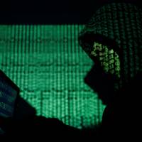 A hooded man holds a laptop computer as cybercode is projected on him in this illustration photo taken Saturday. Some Asian governments, businesses disrupted by cyberattack as authorities brace for more