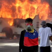 Demonstrators stand next to a buring bus near a protest over Venezuela’s President Nicolas Maduro’s government in Caracas Saturday. As violence rages, Venezuela opposition makes desperate plea to military for dialogue