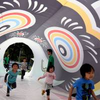 Children walk through a 25-meter long “koinobori,” or carp-shaped streamer, in the Roppongi area of Tokyo’s Minato Ward on Thursday, one day before Children’s Day of May 5. Koinobri is traditionally flown to wish for good health and happiness of children. Population of children sinks to yet another record low