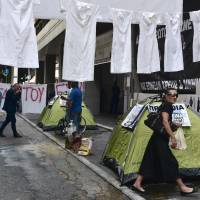 A woman walks by uniforms set up by employees of a public hospital in front of the finance ministry in Athens on Friday during a protest against cuts in health sector. Eurozone ministers struck a long-delayed bailout deal with Greece on Thursday to unlock badly needed rescue cash, but warned that Athens would have to wait for debt relief. Greece wins €8.5 billion in fresh loans though path to debt repayment remains murky