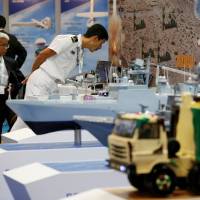 Visitors look at miniature models of military equipment at the Maritime Air Systems and Technologies Asia (MAST) show in the city of Chiba Monday. Kawasaki hamstrung by government stance on military exports