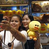 Customers take a selfie with merchandise at Line Village in Bangkok on Thursday. Line Village messaging digital theme park opens in Bangkok