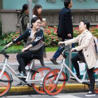Women are seen riding bicycles provided by bike-sharing service Mobike in Shanghai last October. Chinese bicycle-sharing startup Mobike to expand into Japan this year