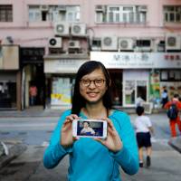 Candy Lau, born five months before Hong Kong’s handover to Chinese rule in 1997, poses on June 6 with a 1997 photo of her taken in the building behind her. Two decades after handover, scant love for China among Hong Kong youth