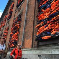 People walk past the new artwork titled ‘Soleil Levant’ (Sunrise in French) by Chinese dissident artist Ai Weiwei, made from over 3,500 lifejackets discarded by migrants on the Greek island of Lesbos, following its official inauguration at Copenhagen’s Kunsthal Charlottenborg museum in Copenhagen Tuesday. Weiwei has barricaded the windows of the museum for his provocative new artwork as a striking reminder of the ongoing migrant crisis, inaugurated Tuesday on World Refugee Day. Ai Weiwei turns migrant lifejackets into artwork near Copenhagen harbor