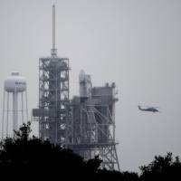 A helicopter flies past the Falcon 9 SpaceX rocket with the first recycled cargo ship that would carry supplies to the International Space Station as it sits on pad 39A moments after the launch was scrubbed because of bad weather at the Kennedy Space Center in Cape Canaveral, Florid, Thursday. SpaceX will make another attempt to launch on Saturday. SpaceX launch scrubbed until Saturday after lightning hits near cape