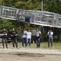 Tsubasa Nakamura (third from left), project leader of Cartivator, watches the flight of the test model of the flying car on a former school ground in Toyota, Aichi Prefecture, on Saturday as another member operates the remote control. Takeoff and cruise: Toyota-backed startup tests ‘flying car’ prototype
