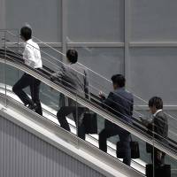 Office workers ride an escalator in Tokyo in June. Japan needs to resolve its severe labor shortage to achieve sustainable economic growth, according to a new government report. Solving Japan's labor shortage will be crucial for sustainable growth: government report
