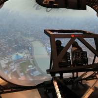 Two people get a virtual reality tour of Tokyo’s Sumida River and Ryogoku Kokugikan on the 8K VR attraction at the National Museum of Emerging Science and Innovation in Koto Ward on Tuesday. NHK develops new VR experience with 8K video projection and hemisphere-shaped screen