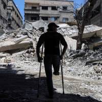 A Syrian amputee uses crutches to walk next to a building that was destroyed following a reported airstrike on the rebel-held town of Ayn Tarma, in Syria’s eastern Ghouta area, on July 14. U.S. special operations chief confirms CIA is ending support for Syria rebels